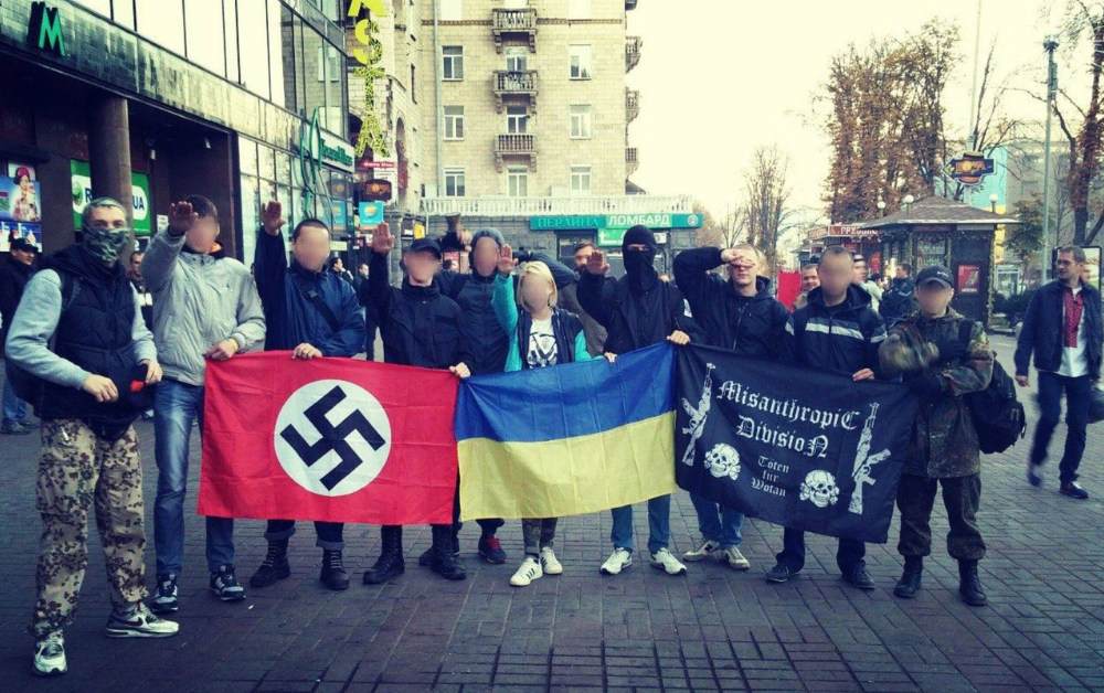 Militanti neonazisti armati con simboli delle SS accanto a una bandiera ucraina sul fronte di guerra